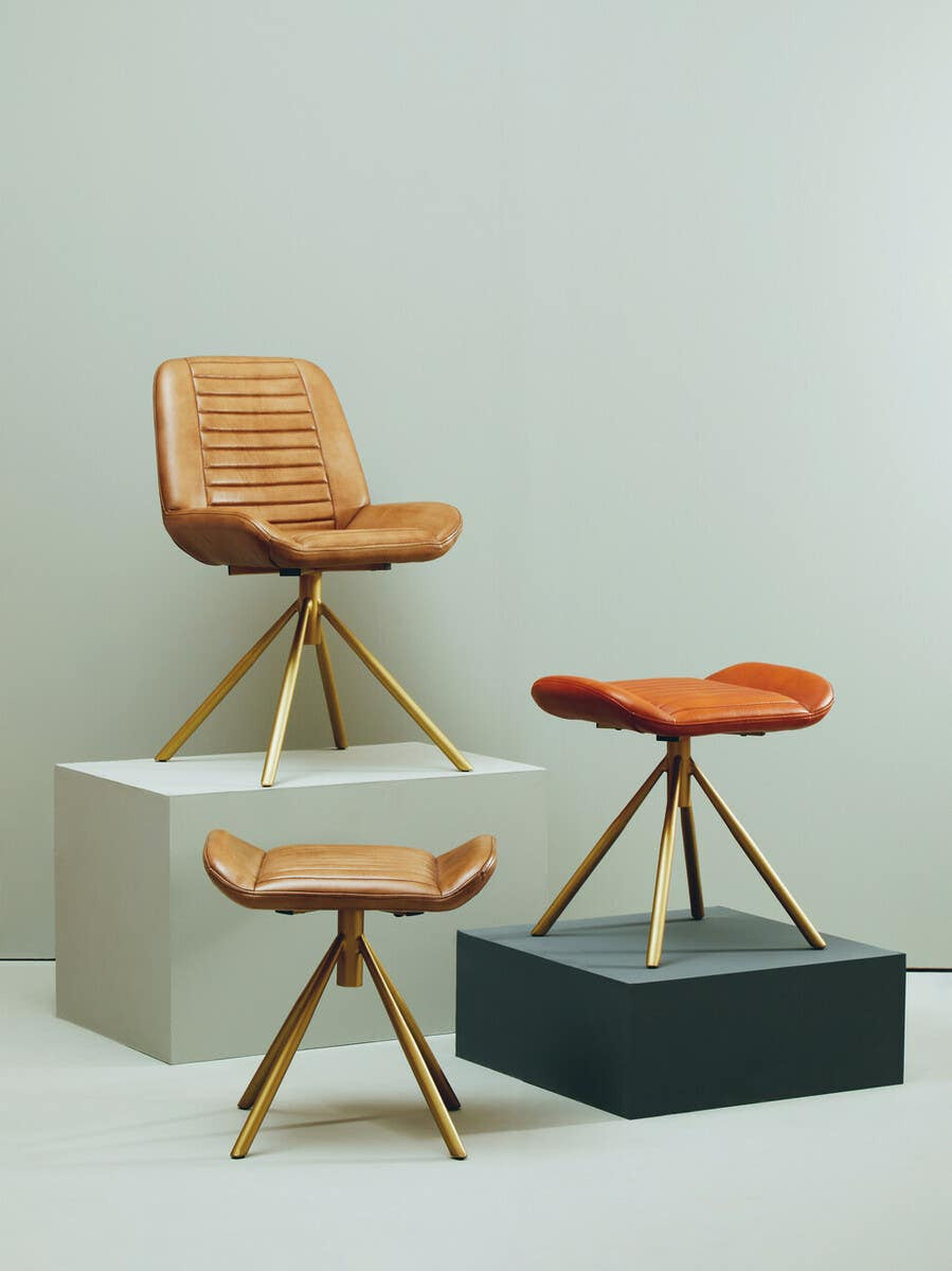 Buffalo tan leather footstool with a sleek design, featuring a cushioned top and wooden legs, displayed alongside a matching chair and another footstool on contrasting pedestals against a neutral background