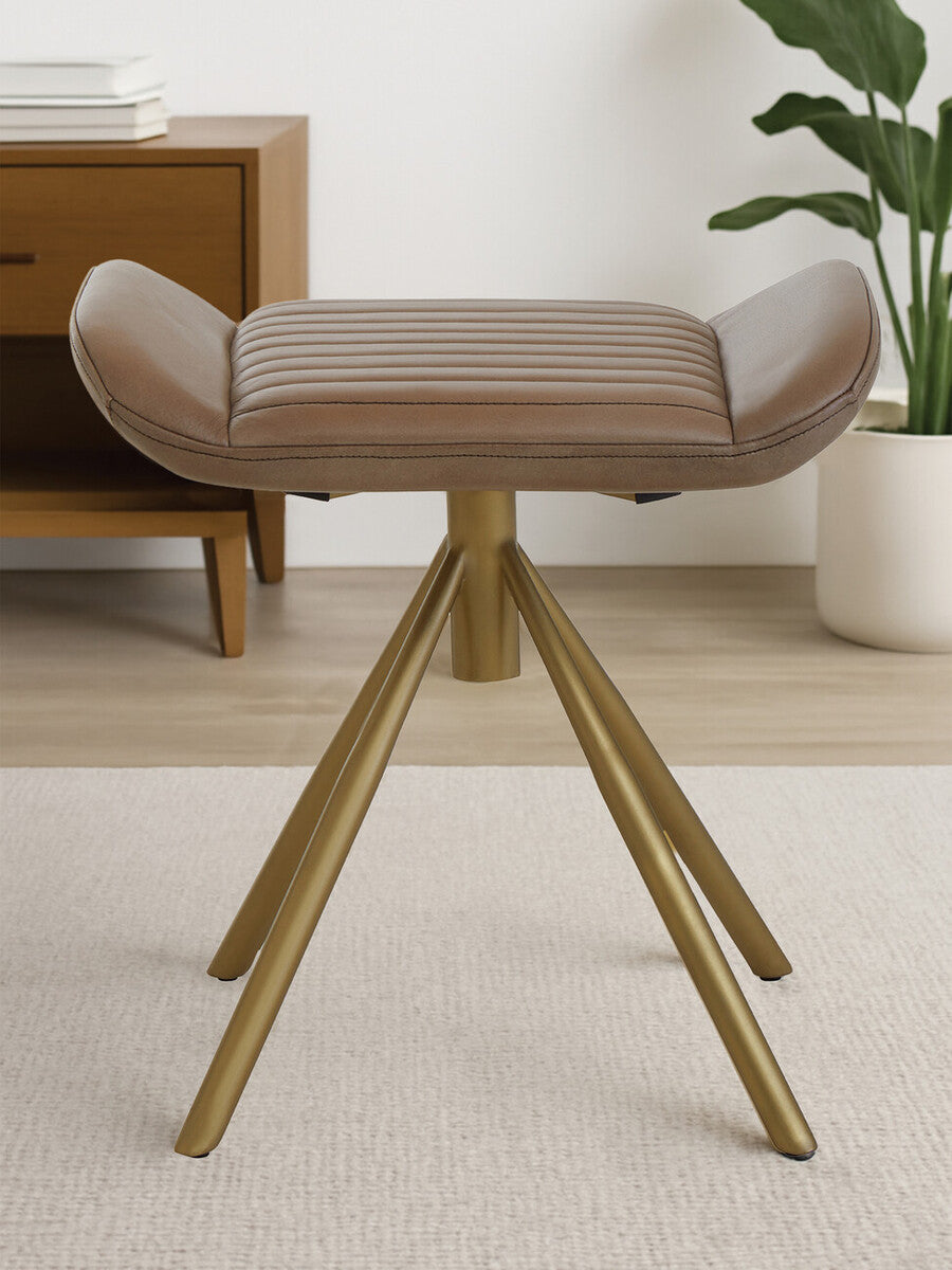 Buffalo grey leather footstool with a cushioned top and natural wood tripod legs, placed on a light-colored rug in a modern living space. A wooden side table and a plant are visible in the background