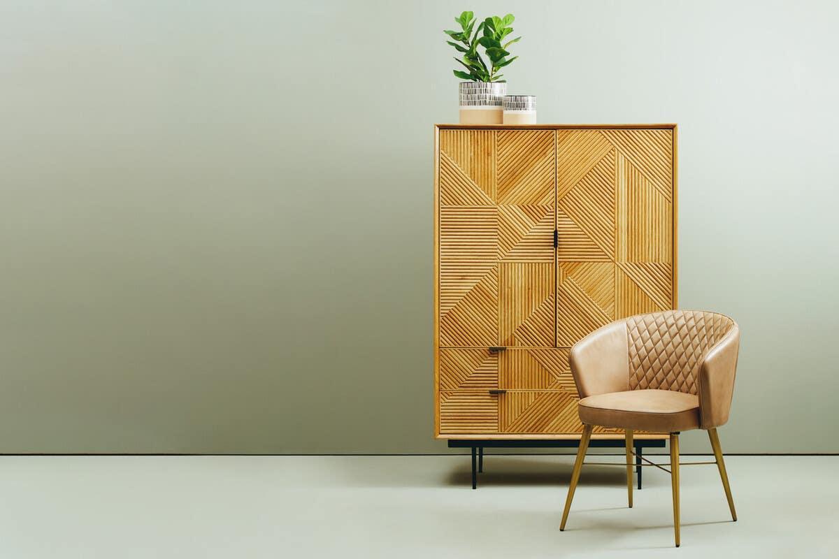 Geometric wood cabinet with potted plants beside tan quilted accent chair on gold legs