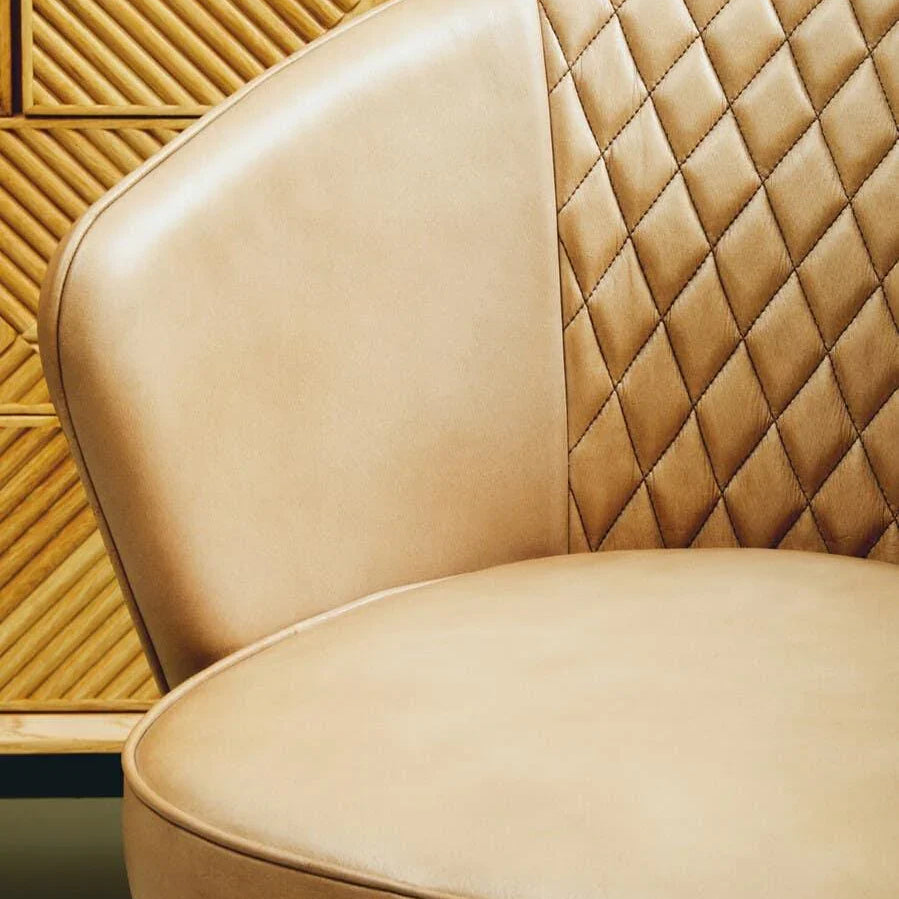 Tan leather accent chair with quilted backrest next to wooden textured cabinet