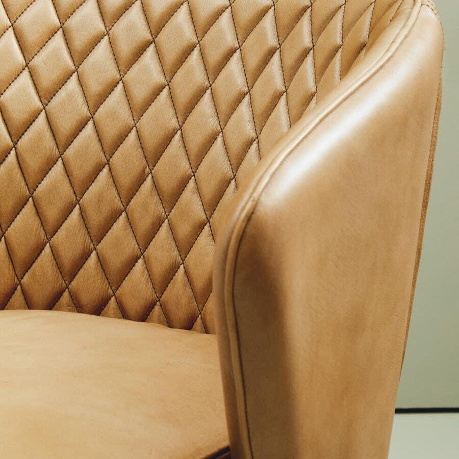 Tan leather armchair with diamond quilted backrest and curved arm design