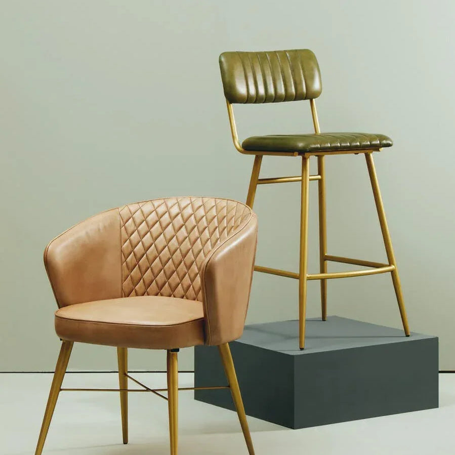 Tan quilted accent chair and green bar stool with gold legs on neutral background
