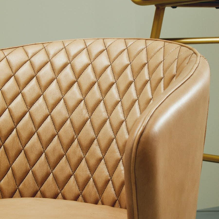 Tan leather armchair with quilted backrest and curved arm in modern interior setting