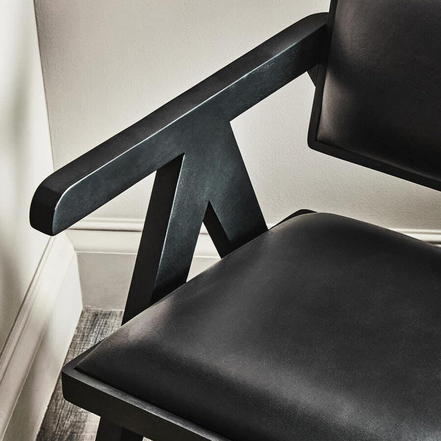 Black leather dining chair with angled armrest and cushioned seat on wood floor