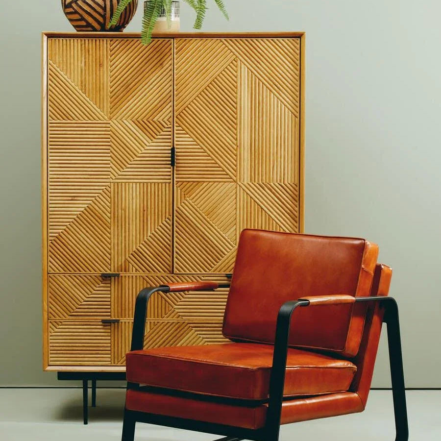 Brown leather armchair with black metal frame in front of geometric wooden cabinet