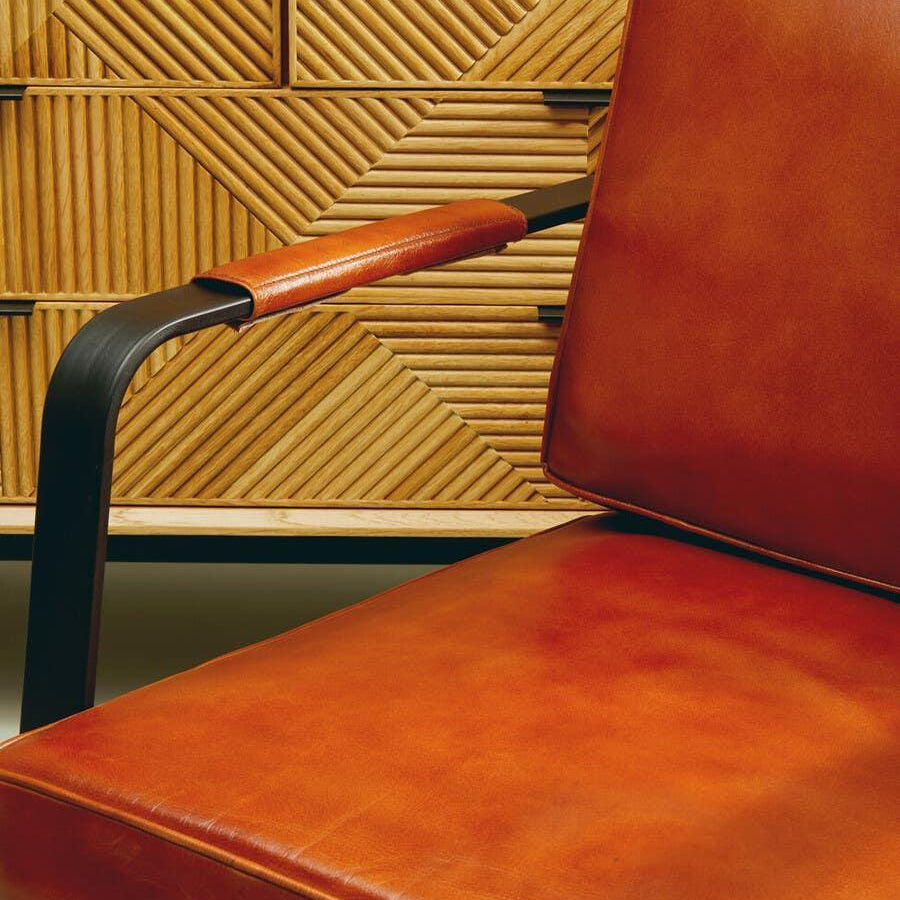 Brown leather armchair with black metal armrest in front of geometric wood paneling