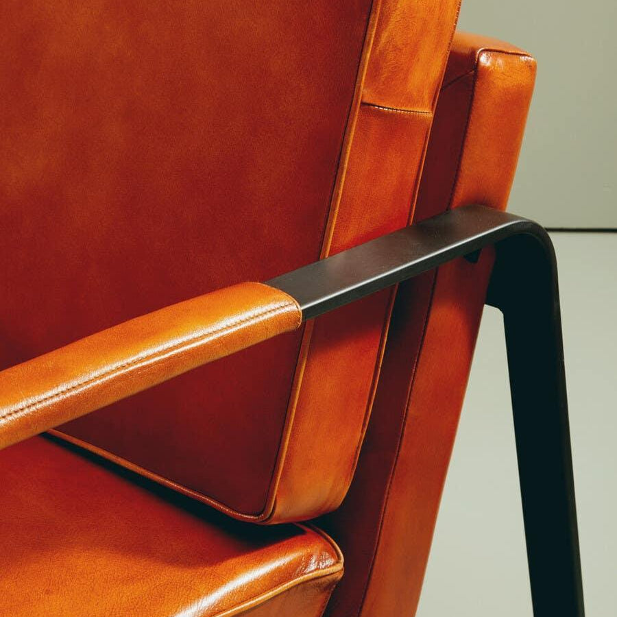 Close-up of orange leather armchair with metal armrest and stitched cushions