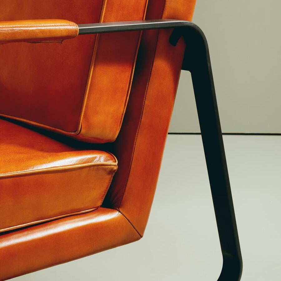 Close-up of modern leather armchair with orange cushions and black metal frame