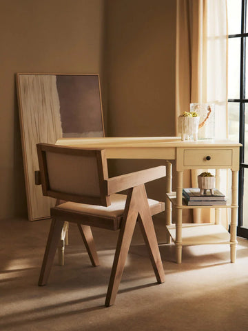 Wooden accent chair with beige upholstery beside cream writing desk in sunlit room