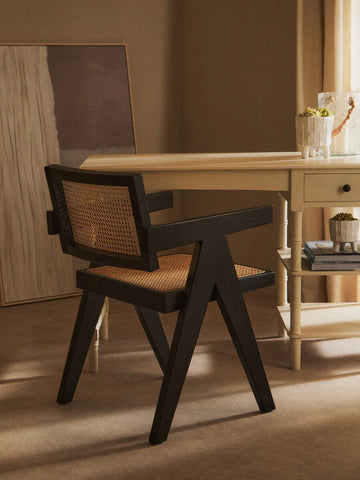 Black wooden dining chair with woven rattan seat beside cream writing desk in neutral room