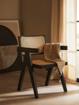 Black wooden accent chair with rattan seat and back, zigzag throw draped over arm