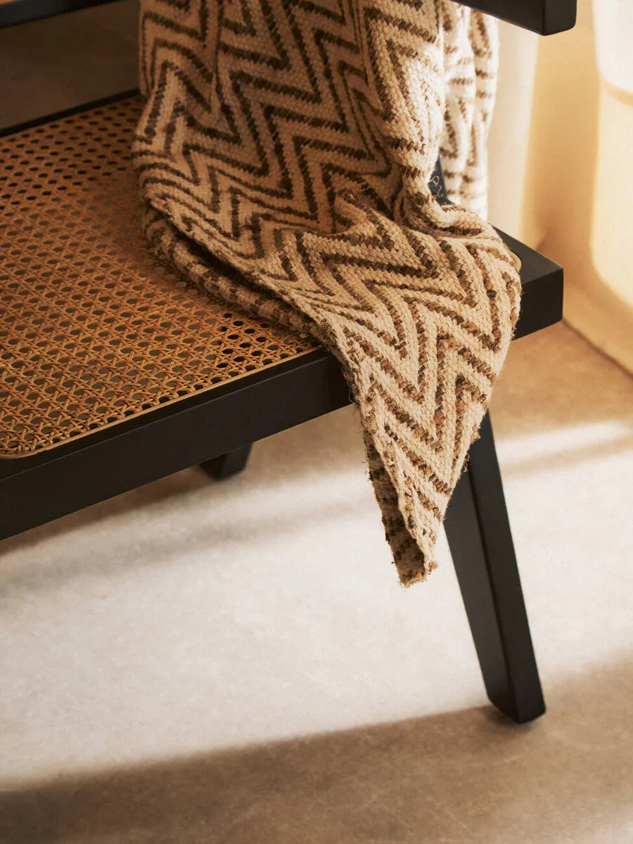 Black wood and rattan bench with chevron patterned throw draped over seat