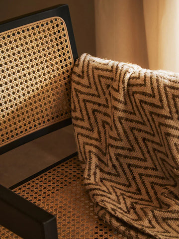 Rattan chair with black frame and zigzag patterned throw draped over backrest