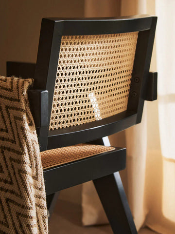 Black wood dining chair with woven cane backrest and seat, draped with a patterned throw