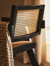 Black wood dining chair with woven cane backrest and seat, draped with a patterned throw