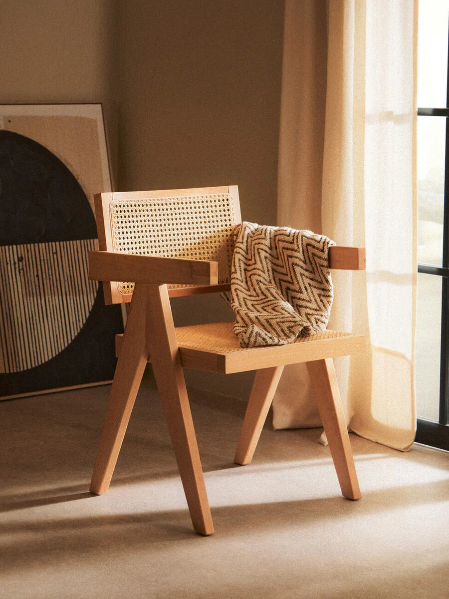 Wooden accent chair with cane backrest and zigzag patterned throw in sunlit room