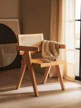 Wooden accent chair with cane backrest and zigzag patterned throw in sunlit room