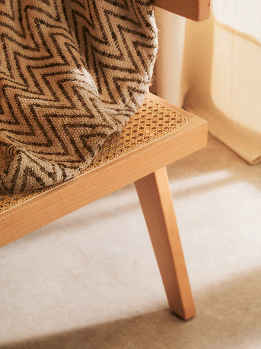 Light wood chair with woven cane seat and herringbone throw in natural room light