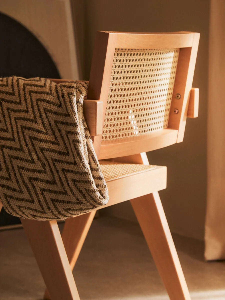 Light wood dining chair with woven cane backrest and chevron throw draped over arm