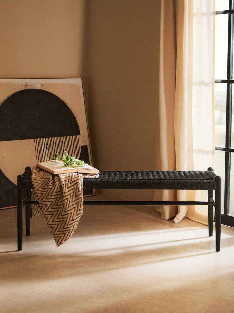 Black woven bench in modern living room with throw blanket, book, and neutral decor
