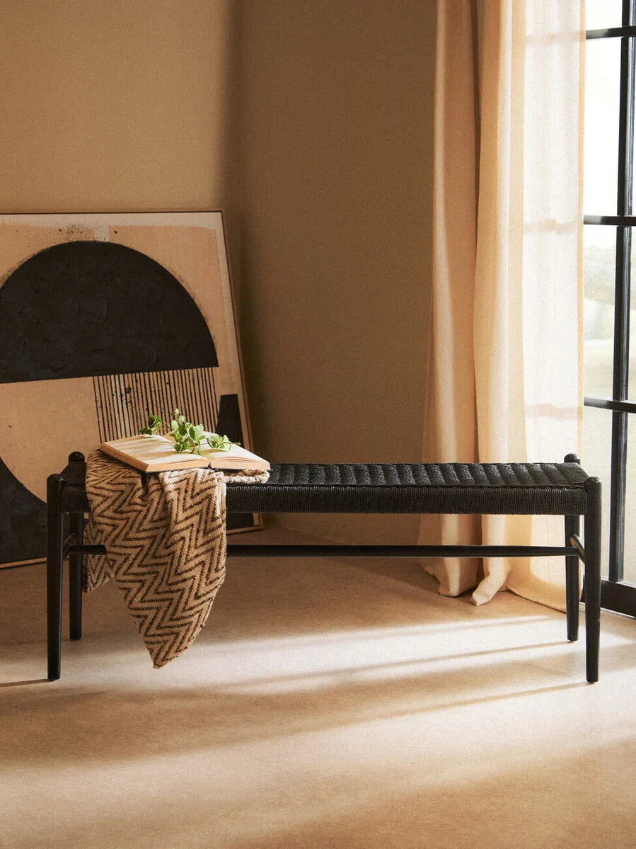 Black woven bench in modern living room with throw blanket, book, and neutral decor