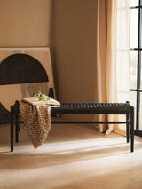 Black woven bench in modern living room with throw blanket, book, and neutral decor