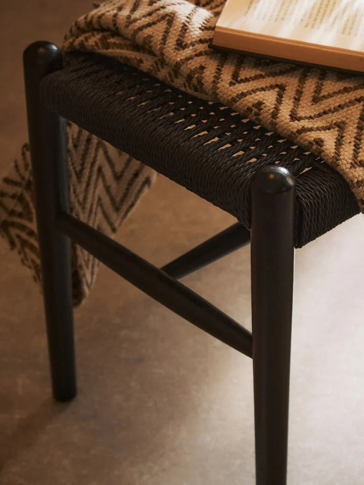 Black woven seat wooden stool with patterned throw and open book