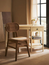 Wooden desk and rattan chair set by window with books and plant decor