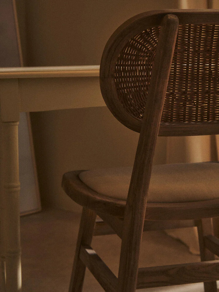Wood dining chair with woven rattan backrest and cushioned seat beside cream table