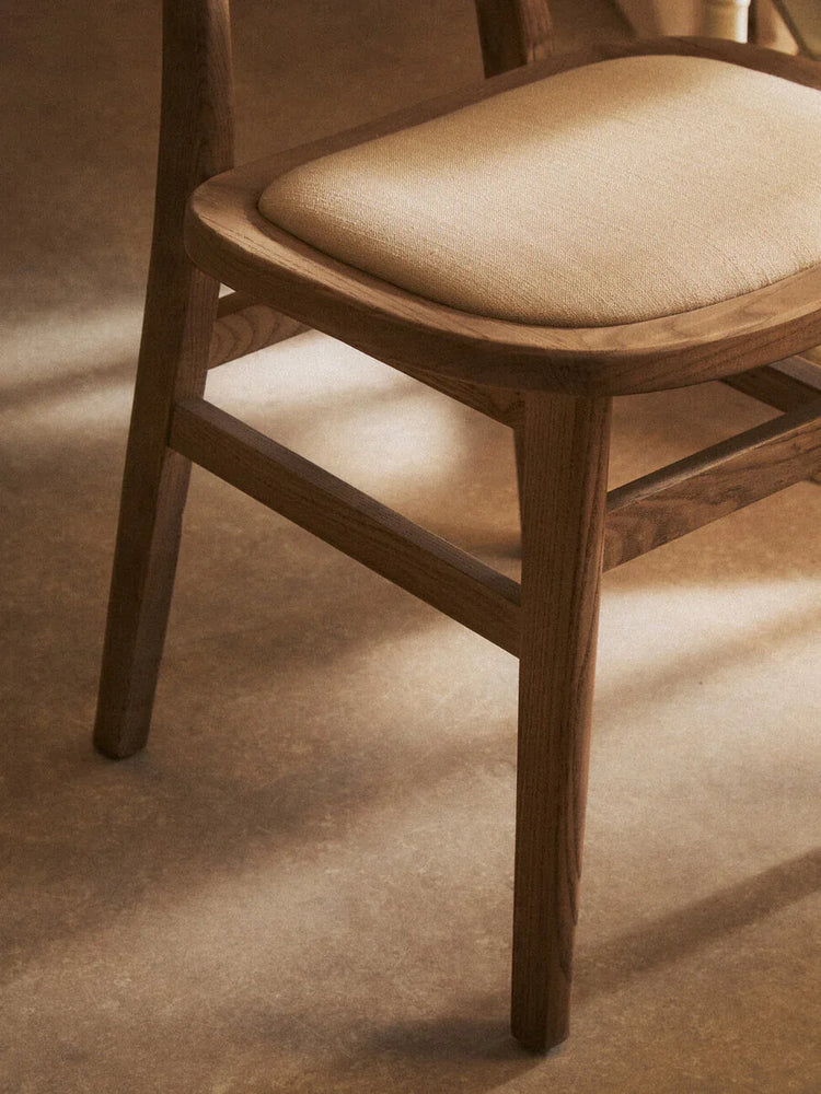 Oak dining chair with light beige fabric seat cushion, side view on wood floor