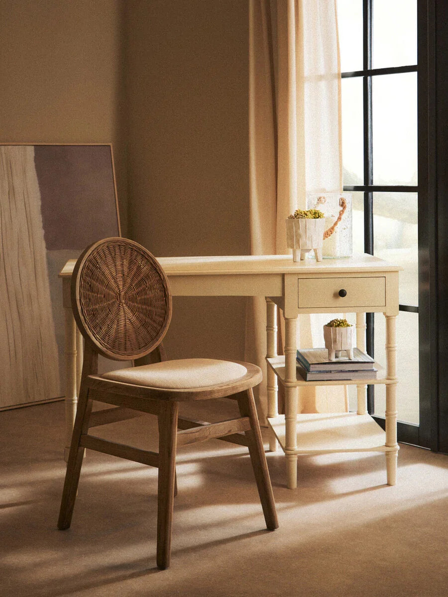 Wooden chair with rattan backrest and cream desk by window with books and potted plant