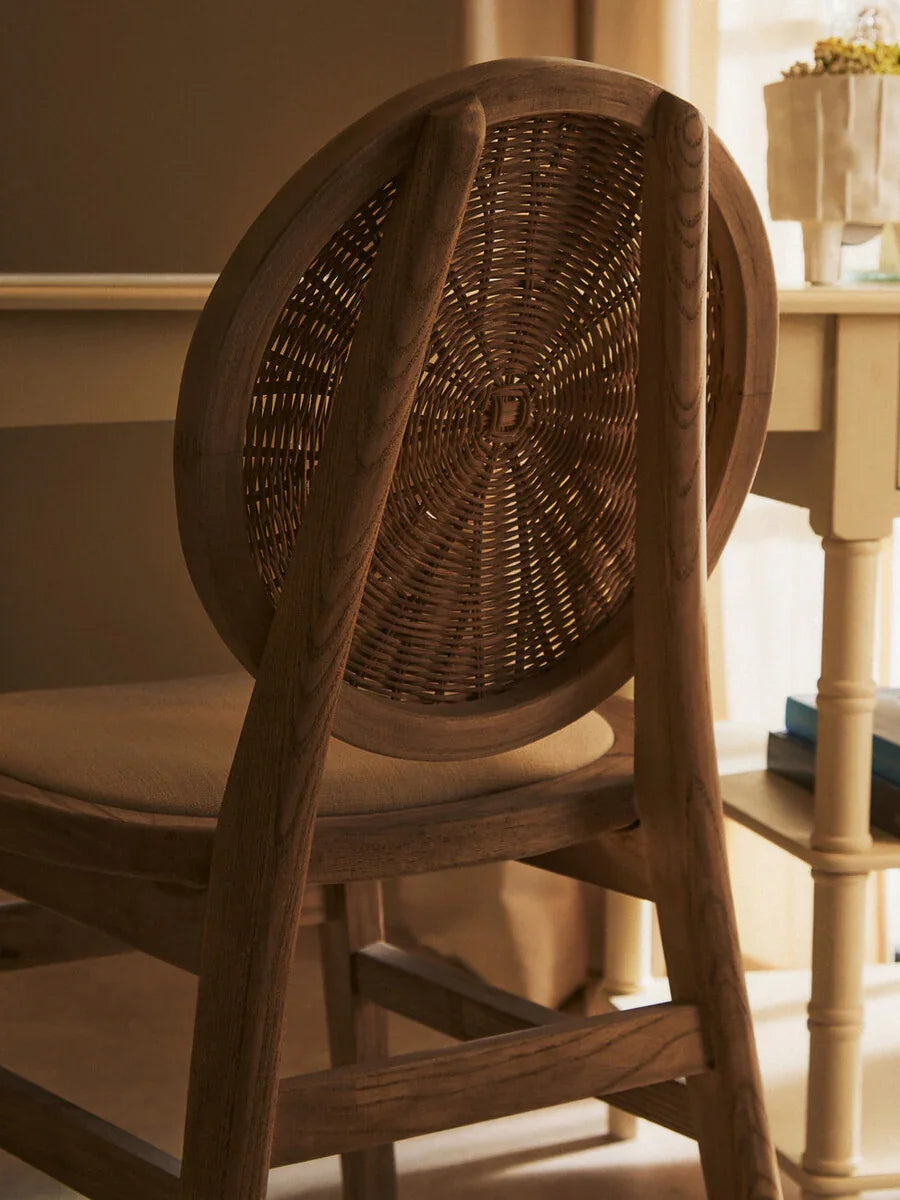 Wooden dining chair with woven rattan backrest and cushioned seat near cream table
