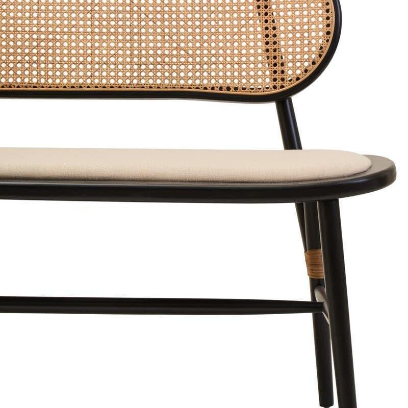 Close up of dining bench with black frame, cane backrest and cream cushioned seat