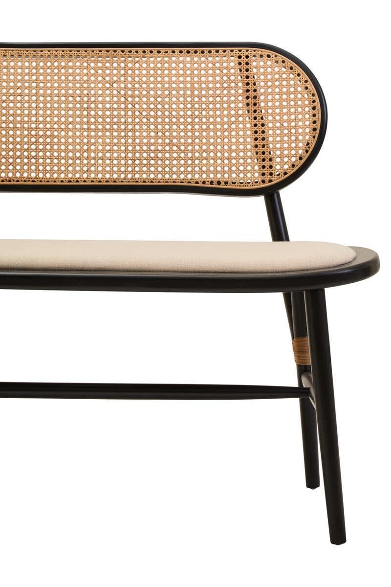 Close up of dining bench with black frame, cane backrest and cream cushioned seat