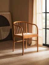 Natural wood dining chair with curved backrest and woven seat by sunlit window