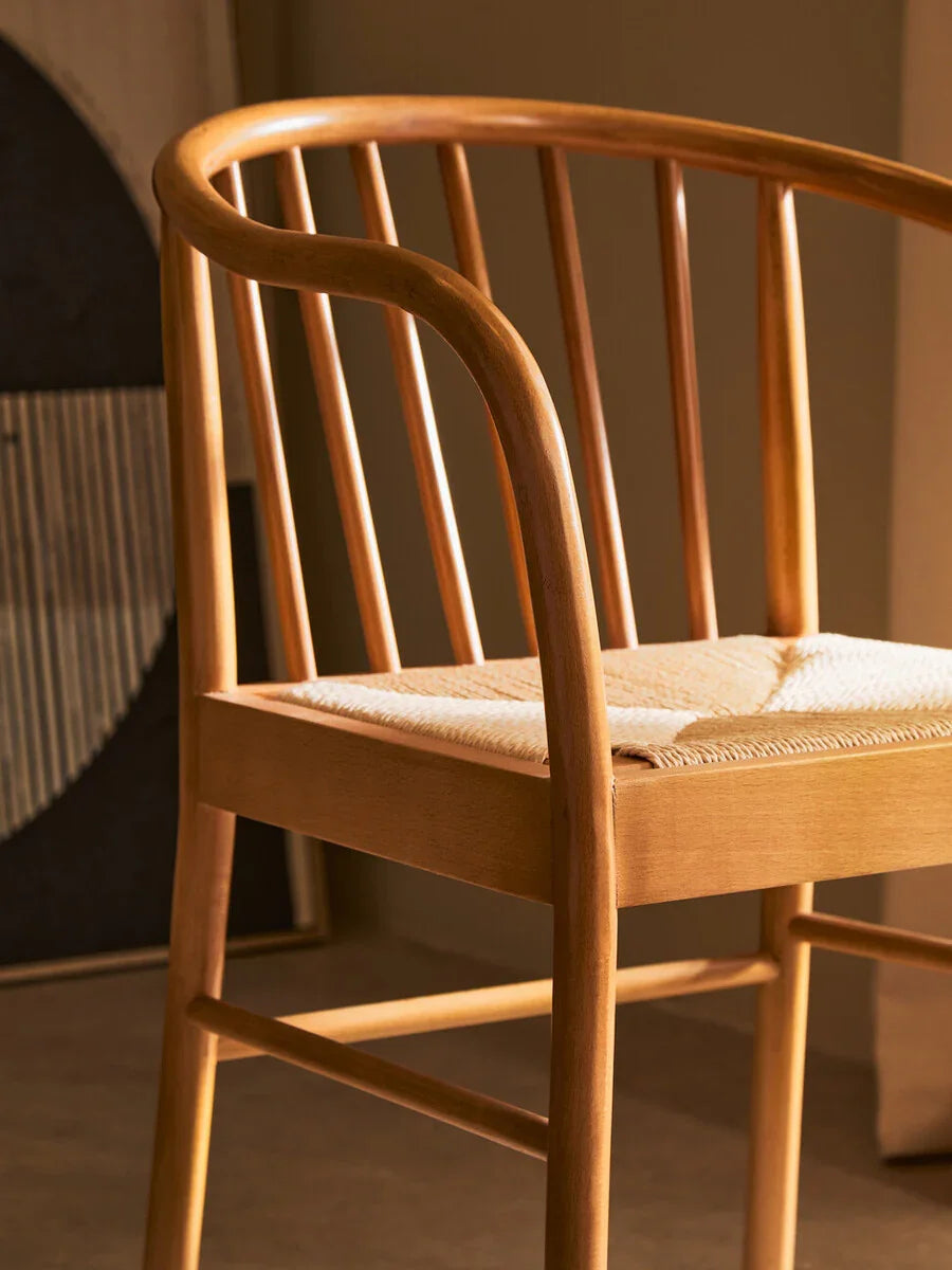 Oak dining chair with curved spindle back and woven seat detail in warm lighting