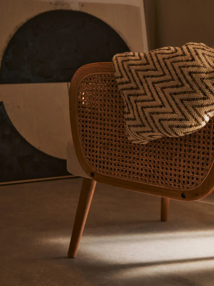 Rattan accent chair with wooden frame and chevron throw blanket in modern living space