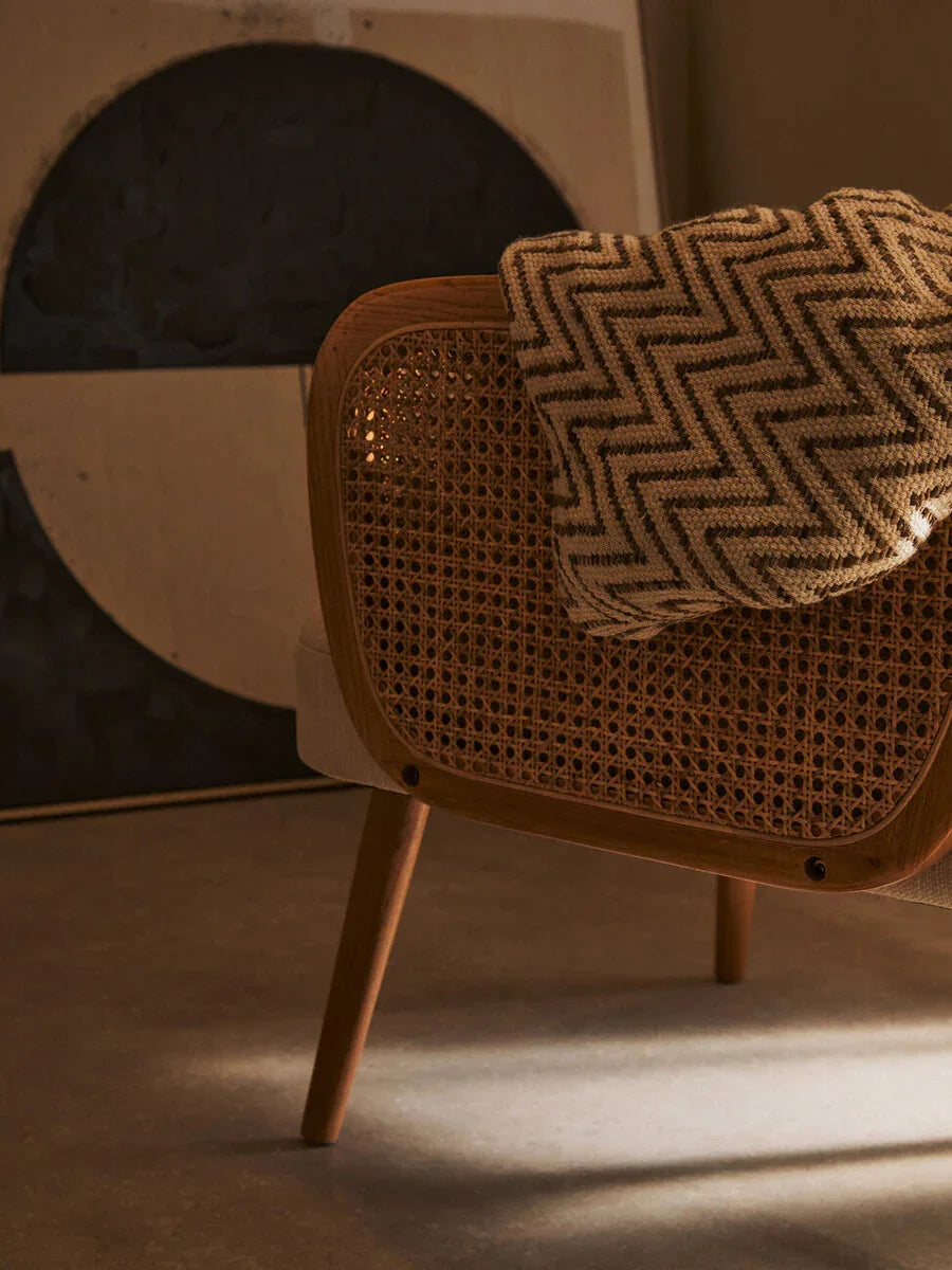 Rattan accent chair with wooden frame and chevron throw blanket in modern living space