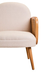 Beige upholstered armchair with wooden armrest and angled wooden legs, close side view