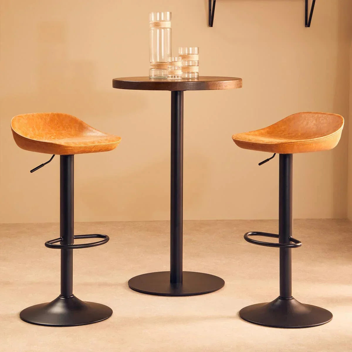 Pair of tan leather bar stools with black metal legs around round wood bar table