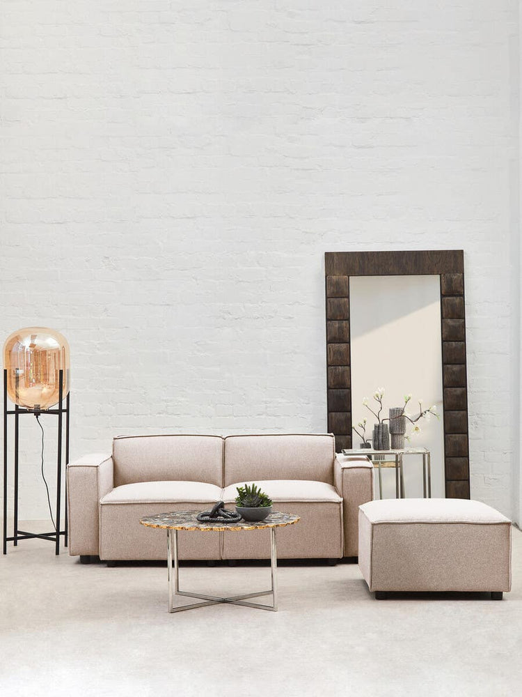 Armless modular sofa in natural fabric, featuring a light beige color, positioned in a modern living space with a large mirror and a decorative lamp on a stand. A small round table with a plant sits in front of the sofa, enhancing the contemporary aesthetic of the room. The walls are painted in a soft, neutral tone