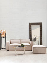 Armless modular sofa in natural fabric, featuring a light beige color, positioned in a modern living space with a large mirror and a decorative lamp on a stand. A small round table with a plant sits in front of the sofa, enhancing the contemporary aesthetic of the room. The walls are painted in a soft, neutral tone