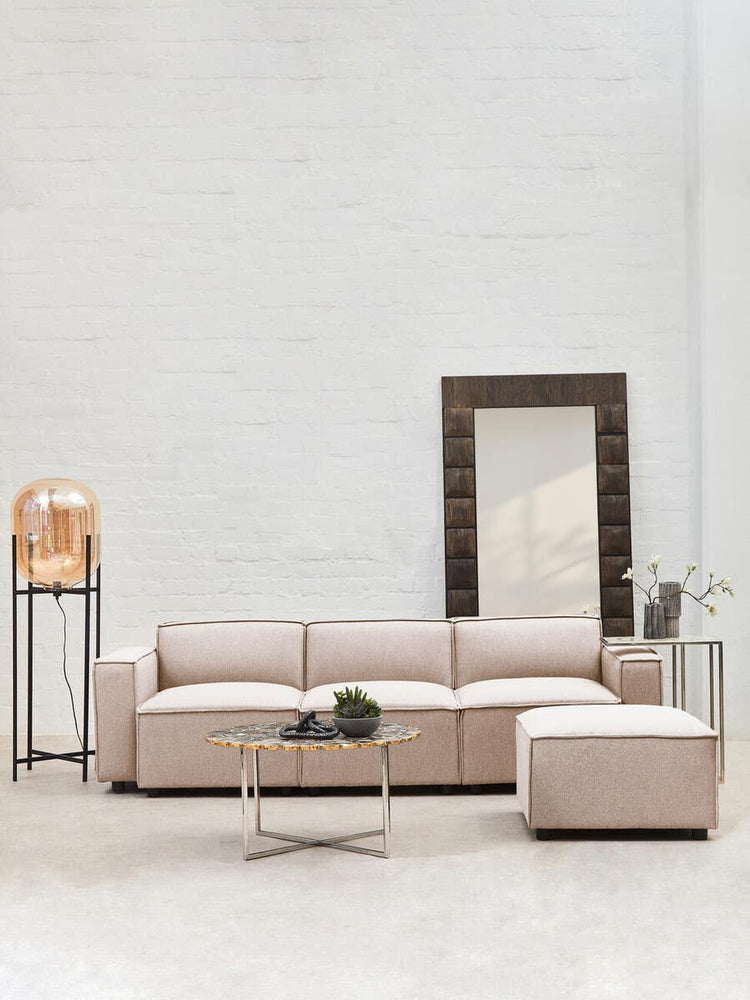 Armless modular sofa in natural fabric, featuring a light beige color, positioned in a bright room with a large mirror and a decorative lamp on a side table. A small green plant is placed on the sofa, complementing the modern aesthetic