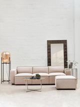 Armless modular sofa in natural fabric, featuring a light beige color, positioned in a bright room with a large mirror and a decorative lamp on a side table. A small green plant is placed on the sofa, complementing the modern aesthetic