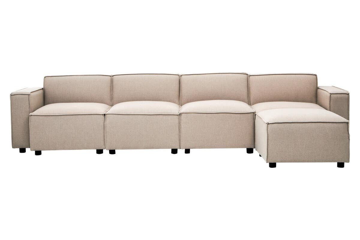 A modular ottoman in a light beige natural fabric, featuring a contemporary design with clean lines and a low profile. The ottoman consists of multiple sections that can be arranged in various configurations, with a smooth surface and subtle stitching details. It rests on small, dark legs for stability