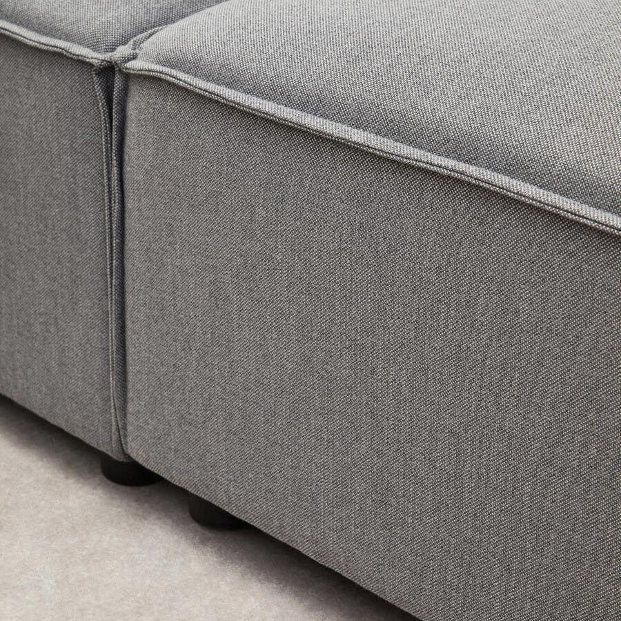 Close-up view of the Toulouse Grey Fabric Right Arm Modular Sofa, showcasing the textured grey fabric upholstery and the clean lines of the sofa's arm and cushion seams. The sofa is positioned on a light-colored floor, highlighting its modern design