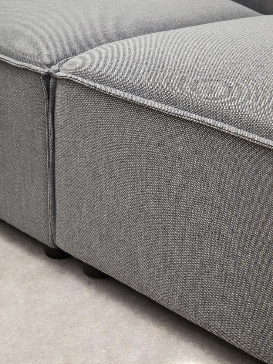 Close-up view of the Toulouse Grey Fabric Right Arm Modular Sofa, showcasing the textured grey fabric upholstery and the clean lines of the sofa's arm and cushion seams. The sofa is positioned on a light-colored floor, highlighting its modern design