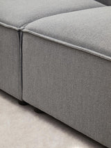 Close-up view of the Toulouse Grey Fabric Right Arm Modular Sofa, showcasing the textured grey fabric upholstery and the clean lines of the sofa's arm and cushion seams. The sofa is positioned on a light-colored floor, highlighting its modern design