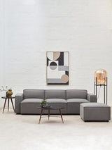 Grey fabric right arm modular sofa with a modern design, featuring clean lines and a low profile. The sofa is positioned in a bright room with a light-colored wall, accompanied by a small round coffee table and a decorative plant. A piece of abstract wall art hangs above the sofa, adding a contemporary touch to the space