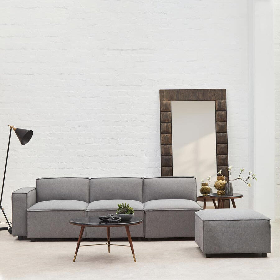 Grey fabric left arm modular sofa with clean lines, positioned in a bright room featuring a large mirror and a floor lamp. A small coffee table with decorative items sits in front of the sofa, and the floor is light-colored, enhancing the airy feel of the space